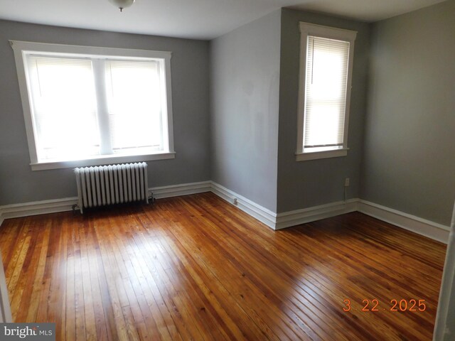 empty room with radiator heating unit, baseboards, and wood-type flooring