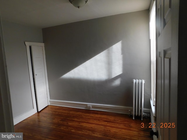 empty room with baseboards, wood finished floors, and radiator heating unit