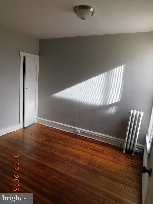 unfurnished room with radiator heating unit, baseboards, and wood finished floors
