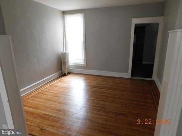 empty room with radiator heating unit, baseboards, and wood finished floors