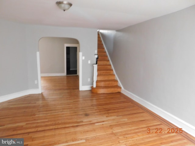unfurnished room with stairway, light wood-type flooring, and baseboards