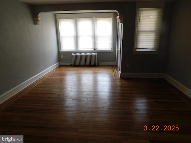 spare room with baseboards, dark wood-style flooring, and radiator heating unit