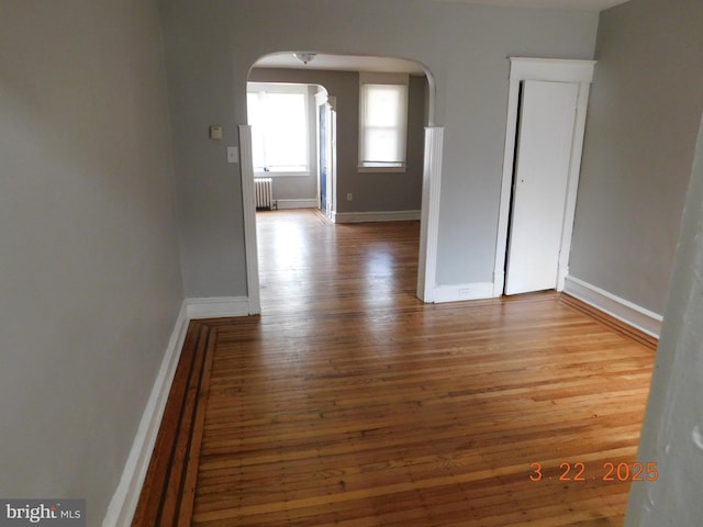 spare room featuring arched walkways, radiator, baseboards, and wood finished floors