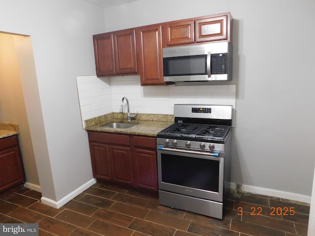 kitchen with tasteful backsplash, baseboards, light stone countertops, stainless steel appliances, and a sink