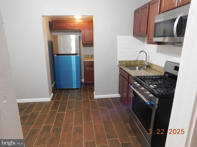 kitchen featuring tasteful backsplash, wood finish floors, light stone counters, appliances with stainless steel finishes, and a sink