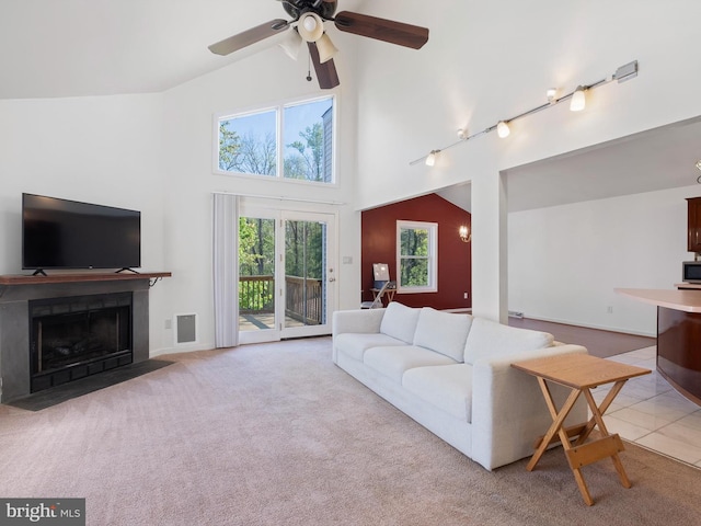 carpeted living area with track lighting, high vaulted ceiling, a ceiling fan, a fireplace with flush hearth, and visible vents