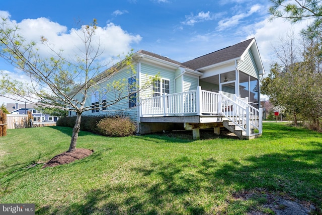 view of side of home with a deck, a ceiling fan, a sunroom, and a lawn