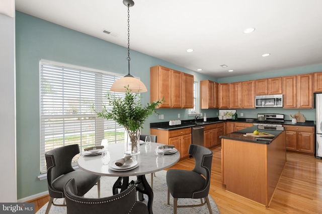kitchen featuring dark countertops, a center island, light wood-style flooring, decorative light fixtures, and appliances with stainless steel finishes