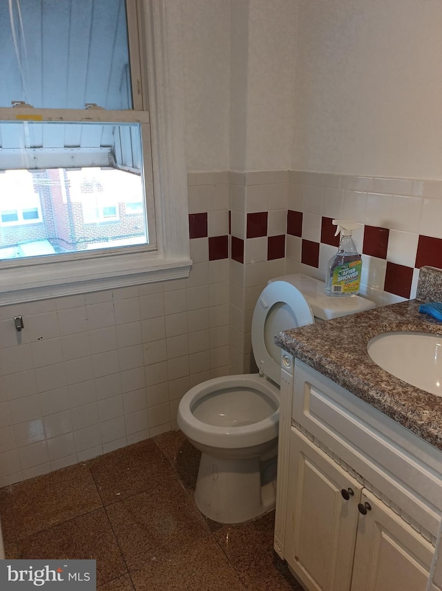 half bathroom featuring toilet, a wainscoted wall, tile walls, and vanity