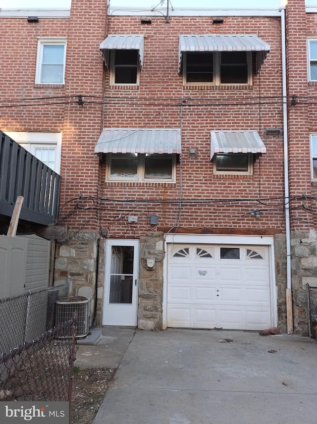 back of house with stone siding, a garage, brick siding, driveway, and cooling unit