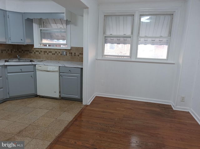 kitchen with light countertops, a sink, backsplash, dishwasher, and baseboards