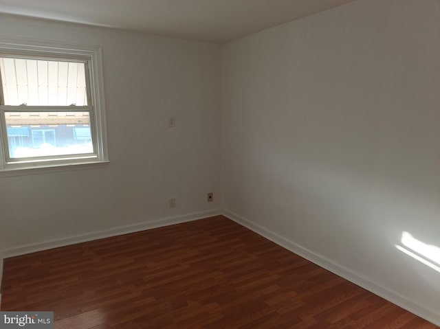 spare room with baseboards and dark wood-style flooring