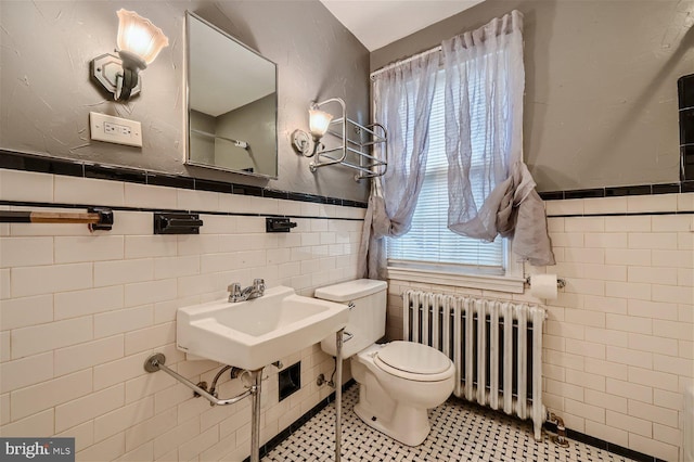 half bathroom with radiator heating unit, tile walls, toilet, a wainscoted wall, and tile patterned flooring