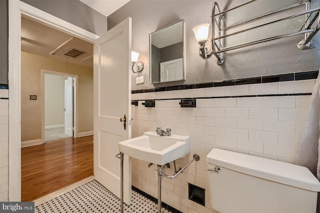bathroom with toilet, tile walls, wood finished floors, and a sink
