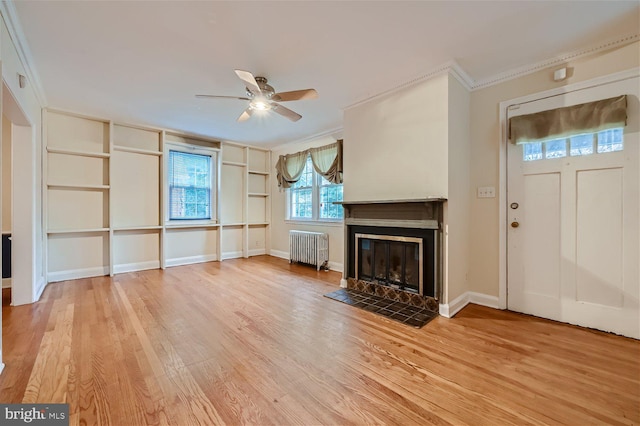 unfurnished living room featuring radiator, crown molding, a ceiling fan, light wood-style floors, and a tiled fireplace