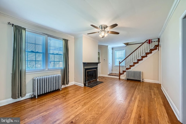 unfurnished living room featuring radiator heating unit, stairs, a fireplace with flush hearth, a ceiling fan, and ornamental molding