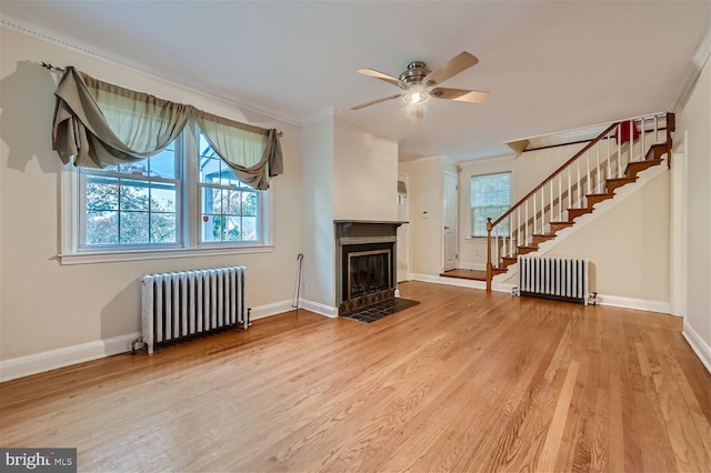 unfurnished living room with radiator heating unit, stairway, crown molding, light wood-type flooring, and a ceiling fan