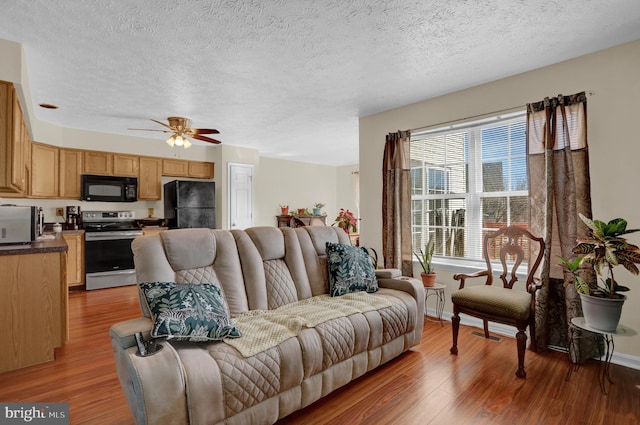 living area featuring a textured ceiling, baseboards, wood finished floors, and a ceiling fan