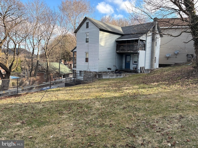 rear view of property featuring a balcony, a shingled roof, fence, and a yard
