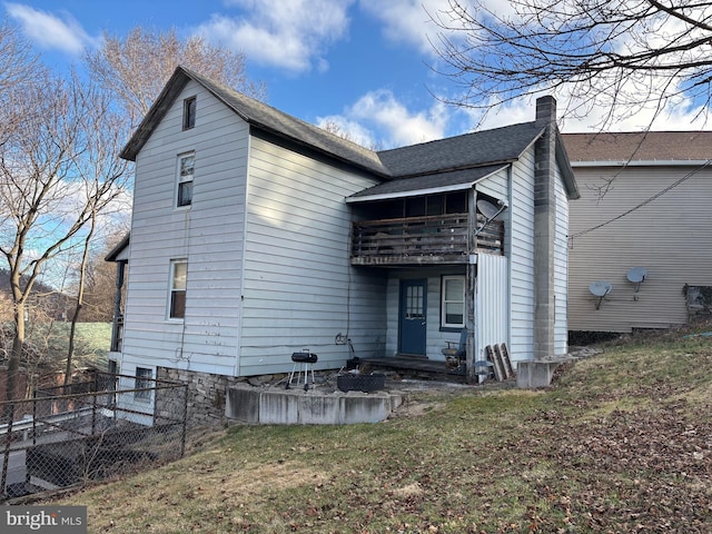 rear view of house with roof with shingles, a lawn, fence, and a chimney