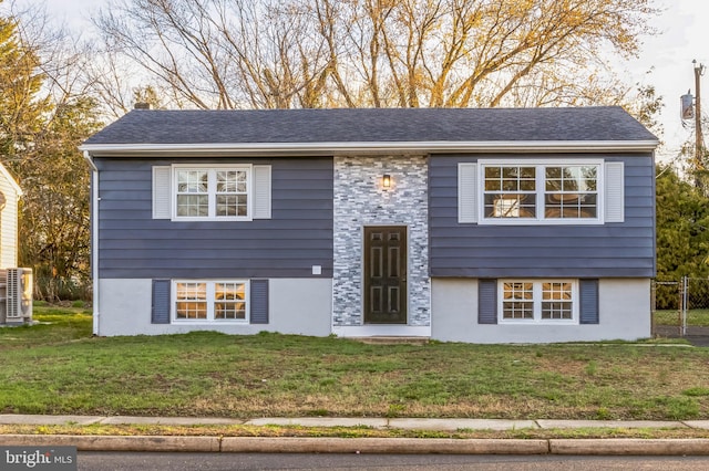 raised ranch featuring a front yard, roof with shingles, stucco siding, and a chimney