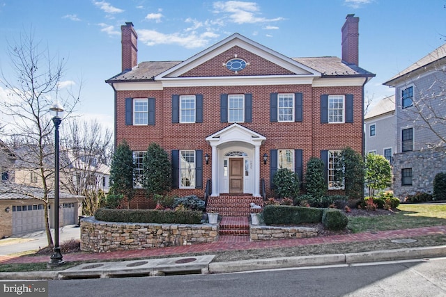 georgian-style home featuring a chimney, an outbuilding, and brick siding