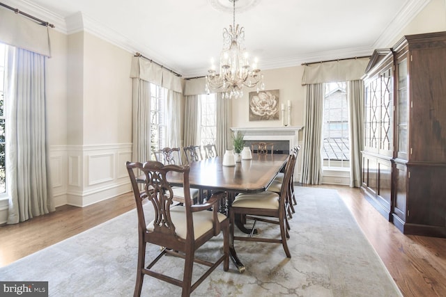dining space featuring an inviting chandelier, ornamental molding, a healthy amount of sunlight, and wood finished floors
