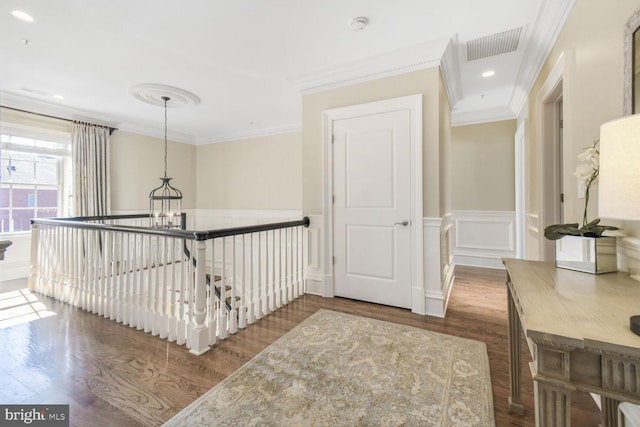 corridor featuring visible vents, wood finished floors, ornamental molding, and wainscoting