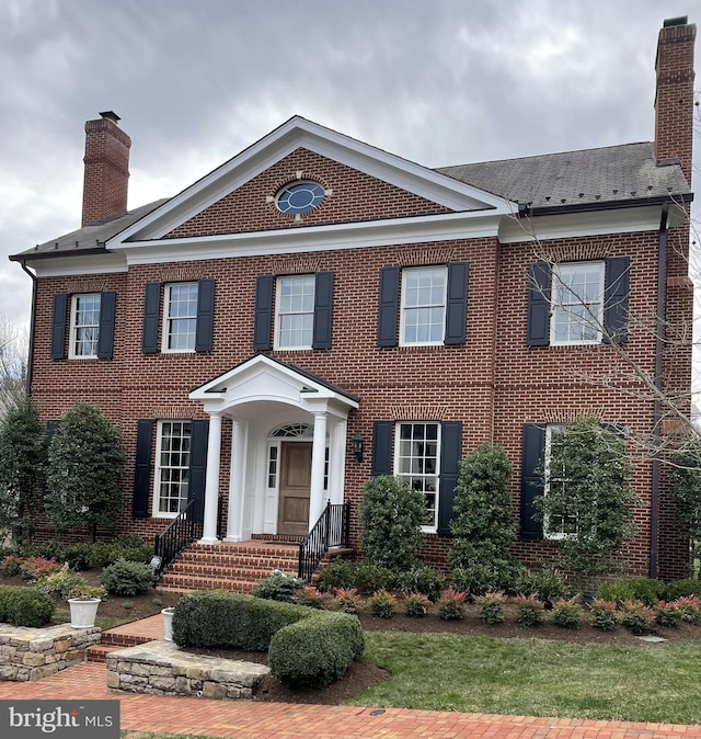 colonial inspired home featuring a chimney and brick siding
