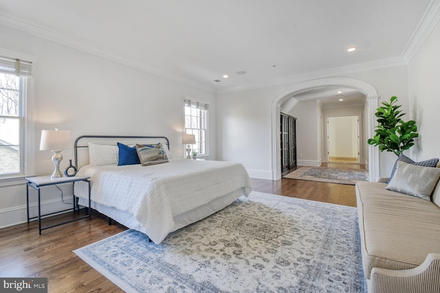 bedroom featuring arched walkways, crown molding, baseboards, and wood finished floors