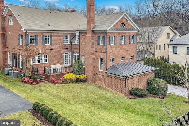 rear view of property featuring a chimney, central air condition unit, brick siding, and a yard