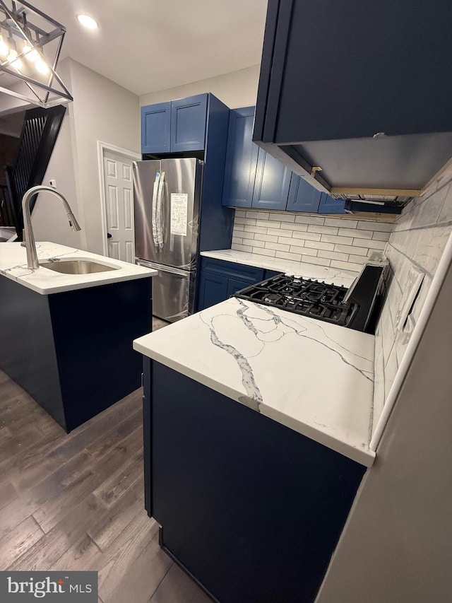 kitchen featuring range hood, freestanding refrigerator, blue cabinets, dark wood-style flooring, and a sink