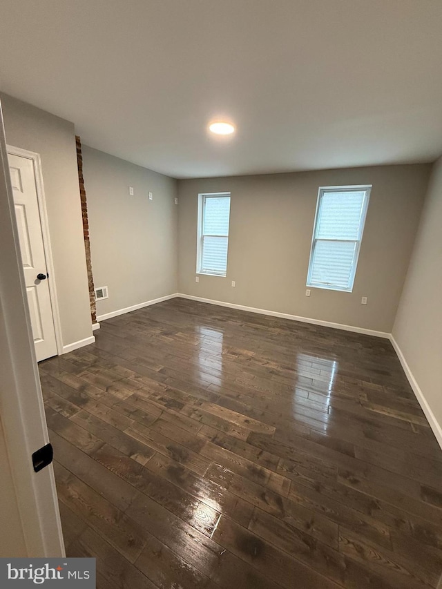 empty room featuring dark wood-type flooring, visible vents, and baseboards