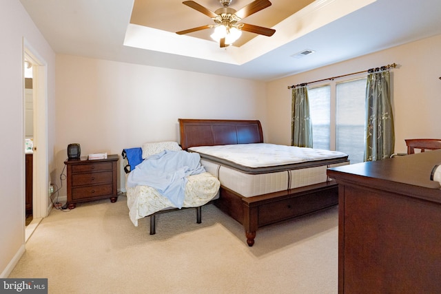 bedroom with a raised ceiling, baseboards, light colored carpet, visible vents, and ceiling fan