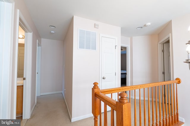 hallway with baseboards, an upstairs landing, visible vents, and light carpet