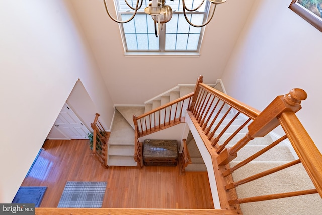 staircase featuring a high ceiling, wood finished floors, and a notable chandelier