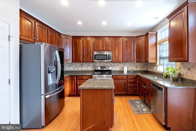 kitchen with light wood-style flooring, stainless steel appliances, tasteful backsplash, a sink, and a center island
