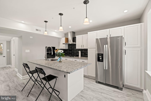kitchen with a sink, light wood finished floors, wall chimney exhaust hood, stainless steel appliances, and visible vents