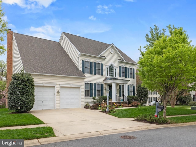 colonial house with a garage, driveway, a shingled roof, a front lawn, and a chimney