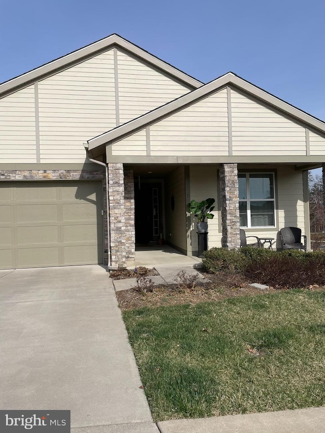view of front of property featuring stone siding, driveway, a front lawn, covered porch, and a garage