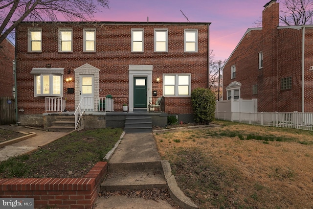 view of front facade featuring brick siding, a lawn, and fence