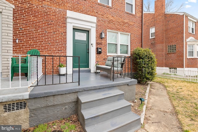 view of exterior entry featuring brick siding and fence