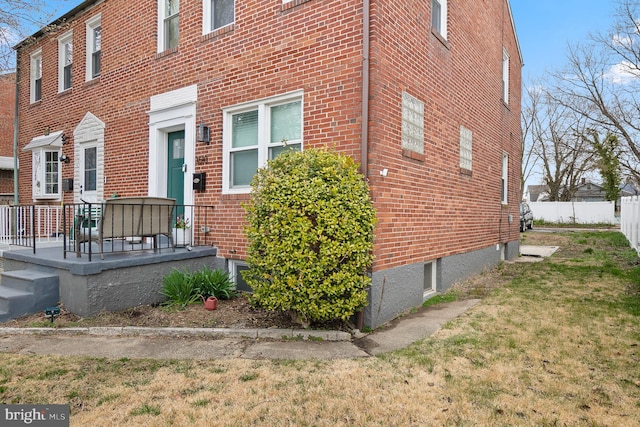 view of side of property with fence, brick siding, and a lawn