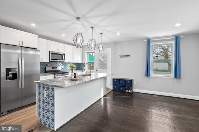 kitchen featuring tasteful backsplash, light stone counters, stainless steel appliances, wood finished floors, and white cabinetry