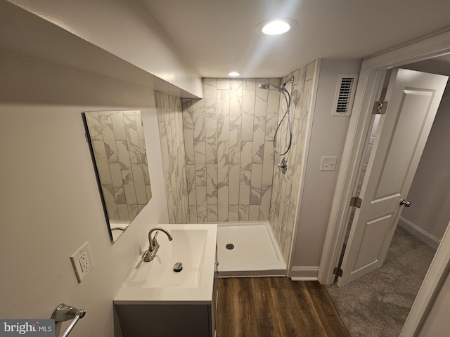 bathroom featuring a tile shower, visible vents, baseboards, wood finished floors, and vanity