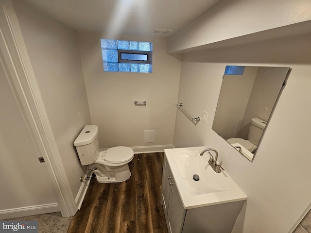 half bathroom with wood finished floors, visible vents, toilet, vanity, and baseboards