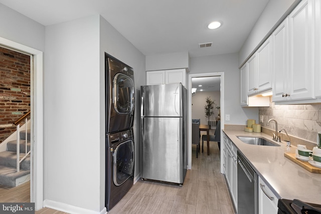 kitchen featuring stacked washer and dryer, light countertops, a sink, light wood finished floors, and stainless steel appliances