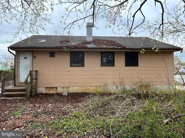 rear view of property with a shingled roof, crawl space, and a chimney
