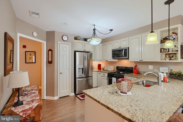 kitchen featuring appliances with stainless steel finishes, a sink, a peninsula, light stone countertops, and light wood-type flooring
