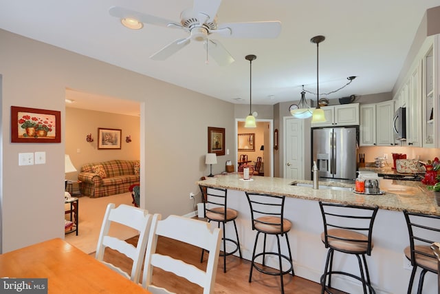 kitchen featuring stainless steel appliances, a peninsula, ceiling fan, light stone counters, and a breakfast bar